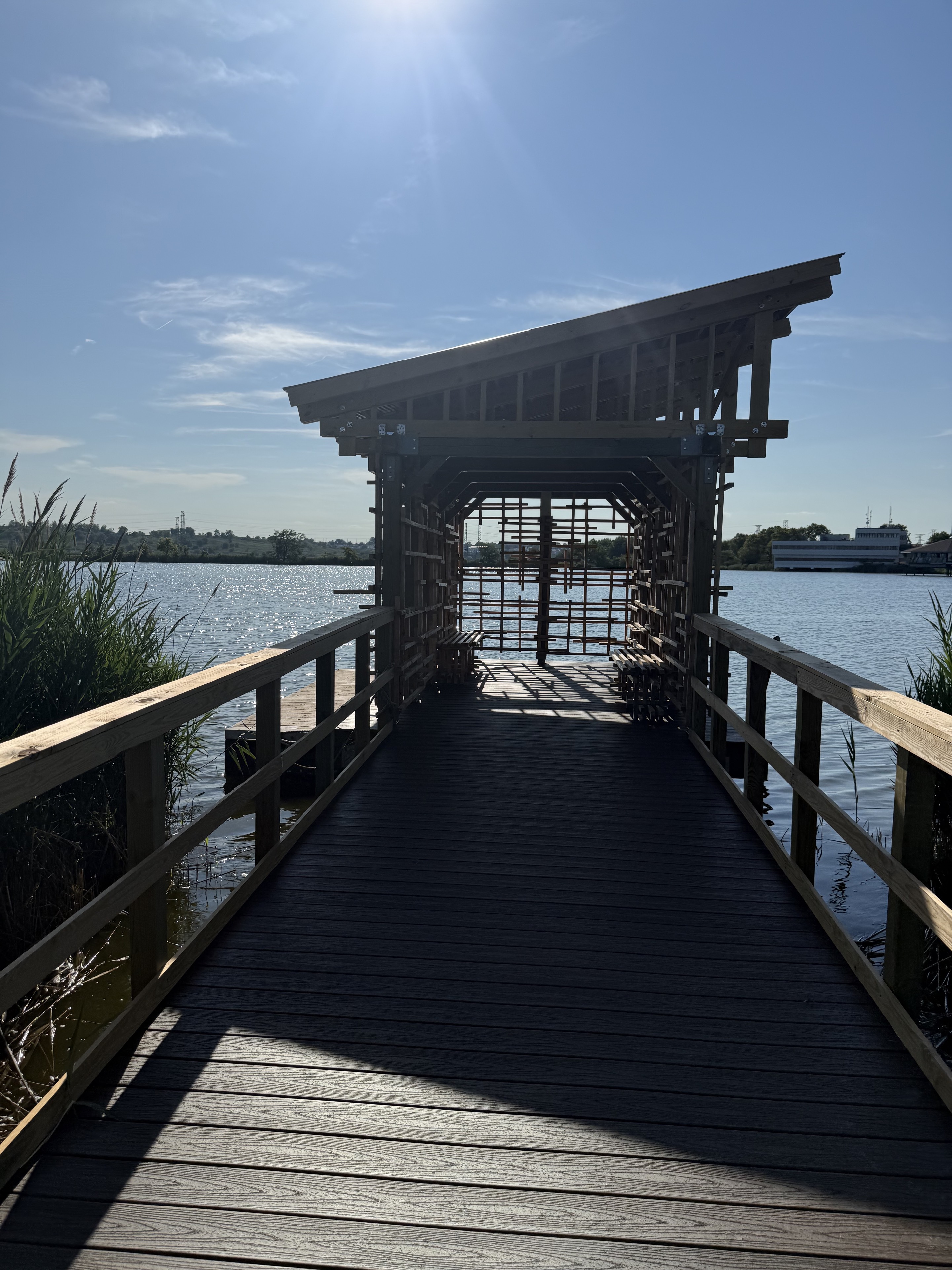 Backlit boardwalk leading into an open timber-lattice bird blind over the water at DeKorte Park.