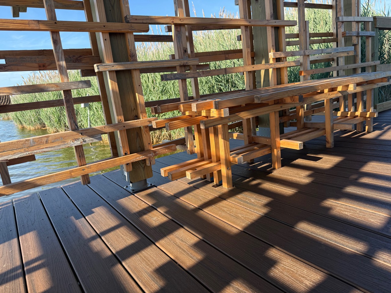 Irregular wood screen and long slatted bench casting a grid of shadows across brown decking.